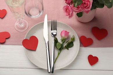 Photo of Romantic place setting with flowers and red paper hearts on white wooden table, above view. St. Valentine's day dinner