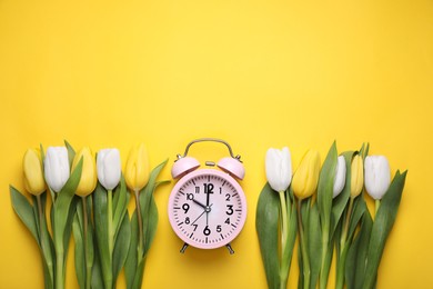 Pink alarm clock and beautiful tulips on yellow background, flat lay with space for text. Spring time