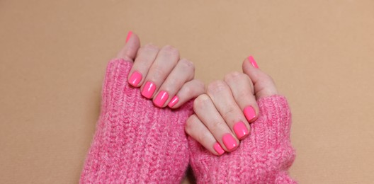 Photo of Woman showing her manicured hands with pink nail polish on dark beige background, closeup