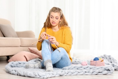 Photo of Young woman in cozy warm sweater knitting with needles on floor at home. Space for text