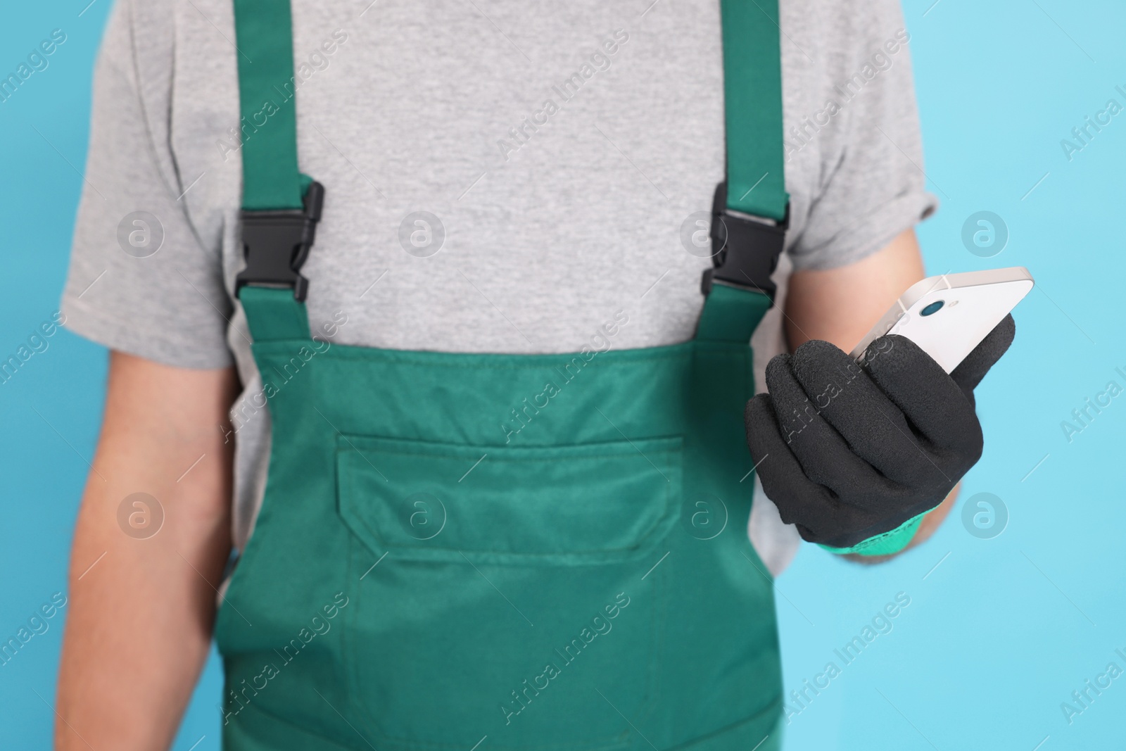 Photo of Professional repairman in uniform with phone on light blue background, closeup