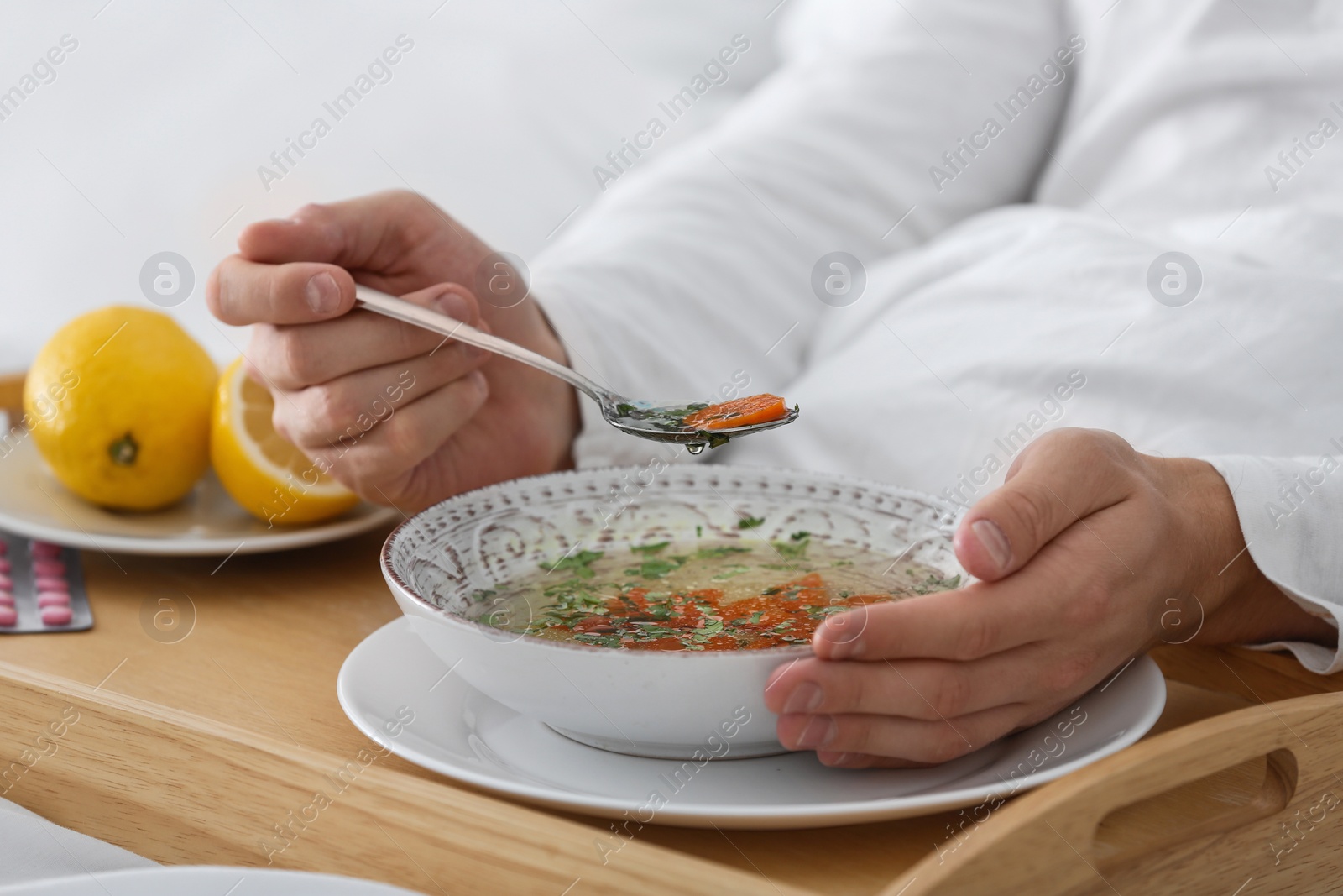 Photo of Sick young man eating soup to cure flu in bed at home, closeup