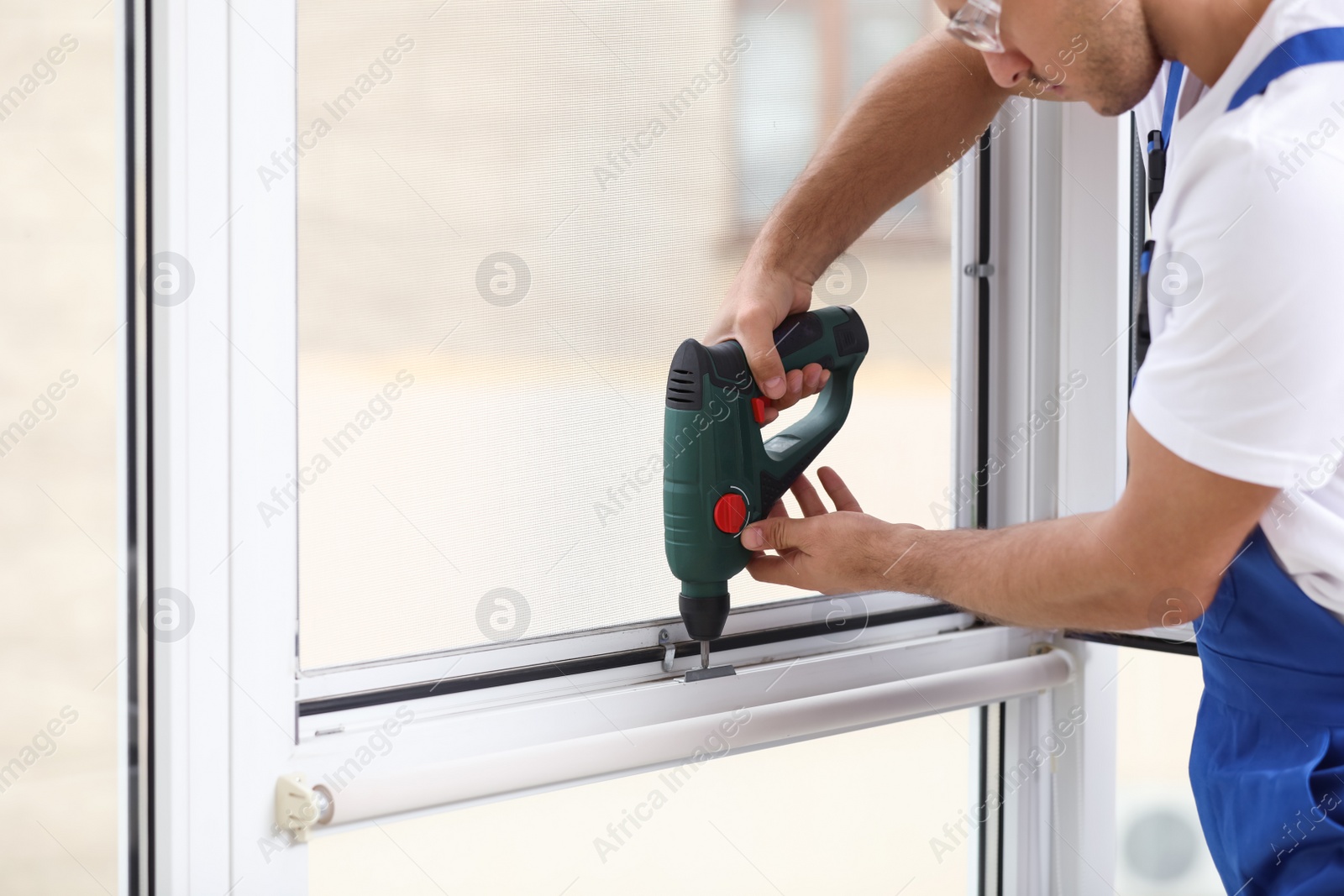 Photo of Construction worker repairing plastic window with electric screwdriver indoors