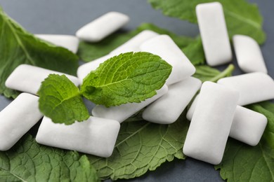 Photo of Tasty white chewing gums and mint leaves on grey background, closeup