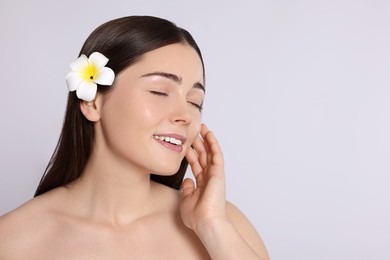 Photo of Young woman with plumeria flower in hair on light grey background, space for text. Spa treatment