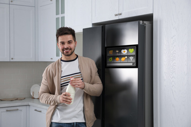 Image of Young man with bottle of milk near smart refrigerator in kitchen