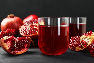 Photo of Tasty pomegranate juice in glasses and fresh fruits on black wooden table, closeup