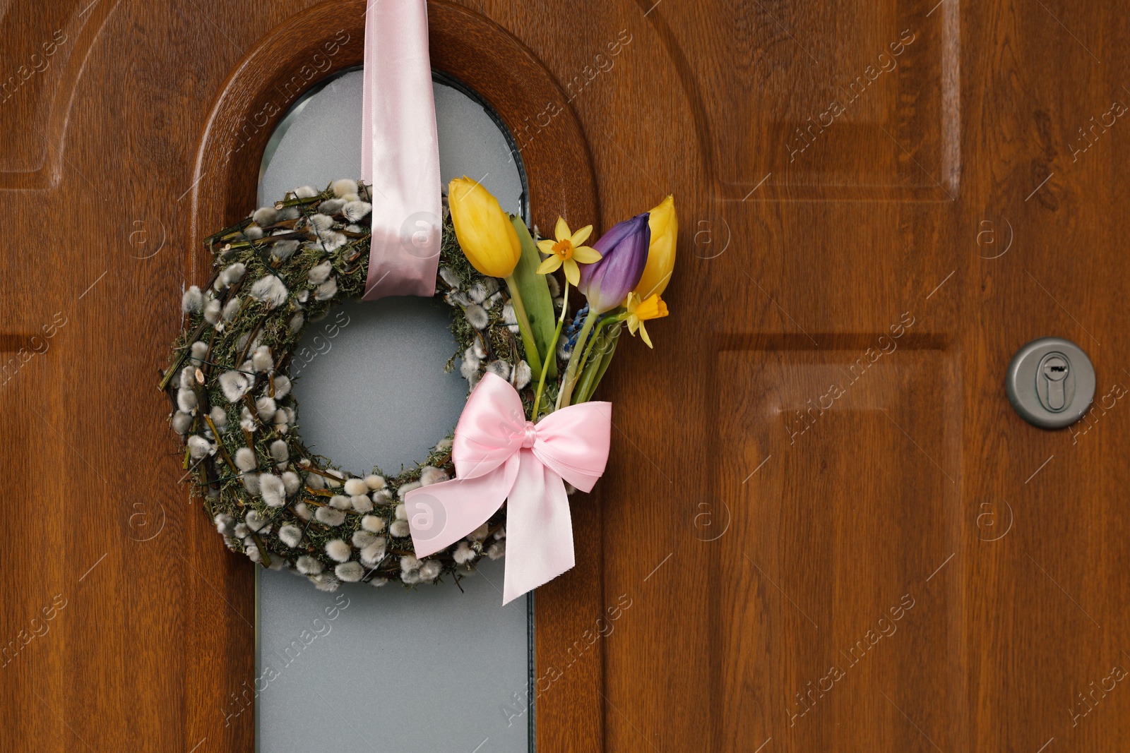 Photo of Wreath made of beautiful willow branches, pink bow and colorful tulip flowers on wooden door, space for text