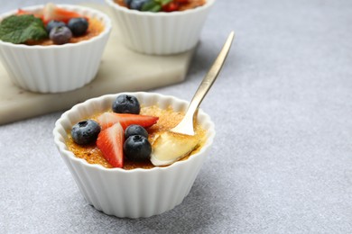 Photo of Delicious creme brulee with berries in bowl and spoon on grey textured table. Space for text