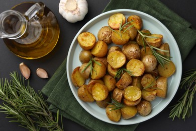 Delicious baked potatoes with rosemary and ingredients on black table, flat lay