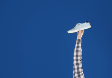 Photo of Young man holding comfortable shoe on blue background, closeup. Space for text