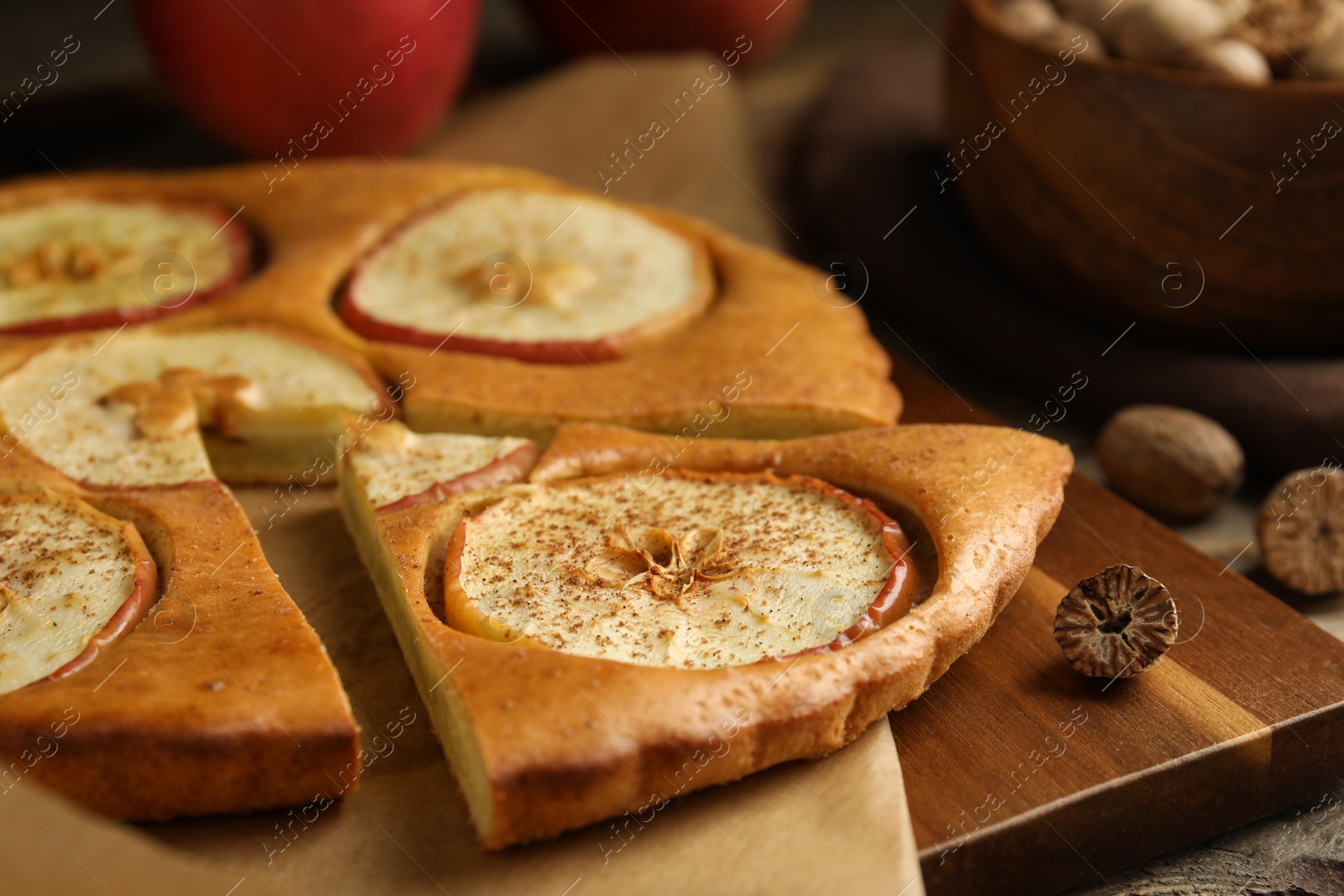 Photo of Nutmeg seeds and tasty apple pie on wooden board, closeup