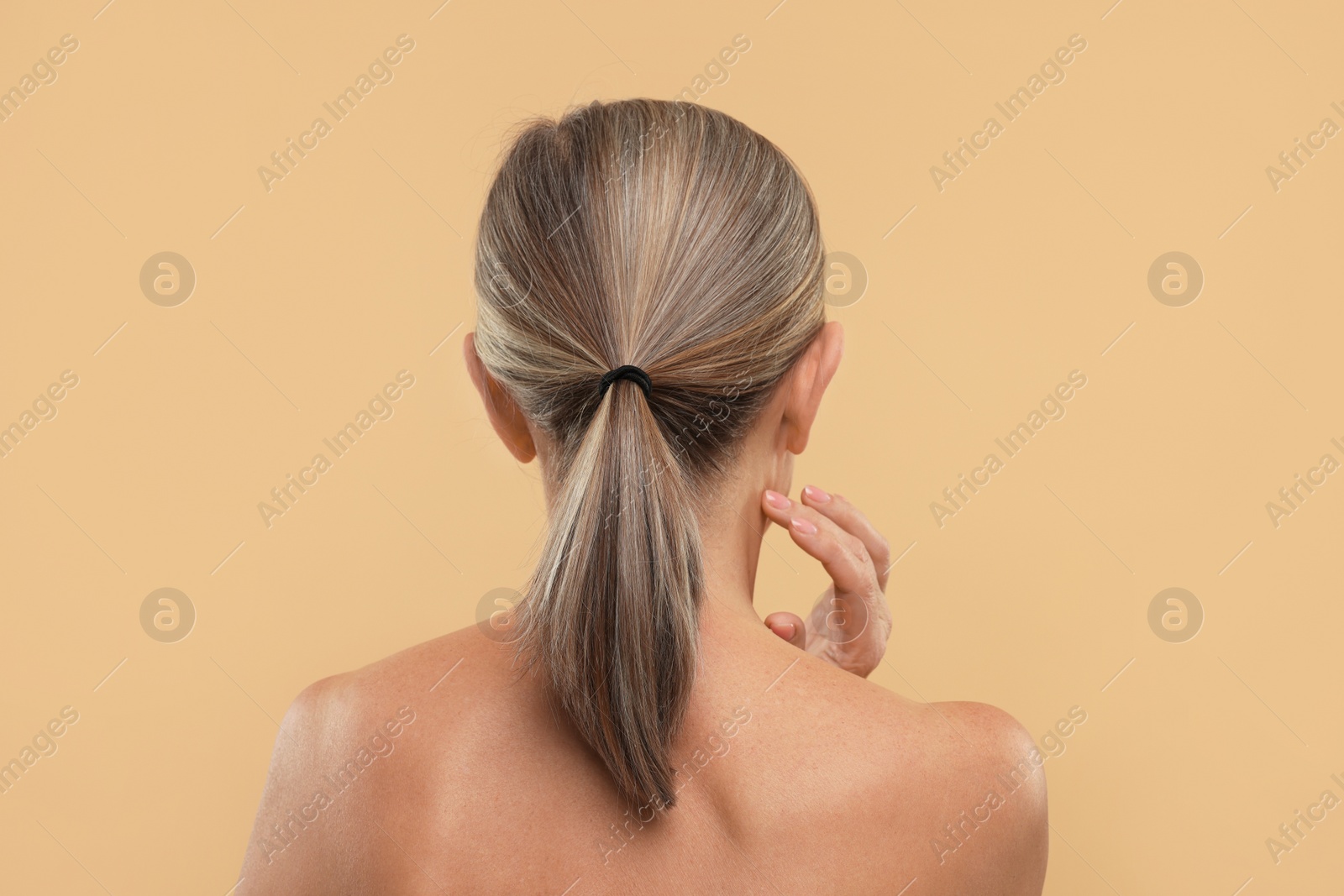Photo of Mature woman touching her neck on beige background, back view