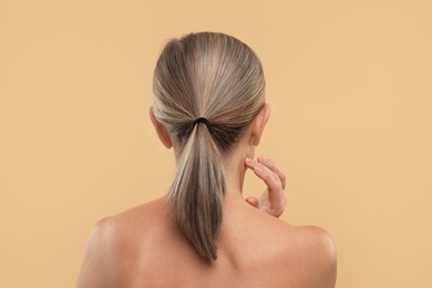 Mature woman touching her neck on beige background, back view