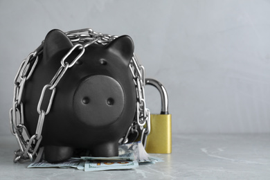 Photo of Piggy bank with steel chain, padlock and banknotes on grey marble table, space for text. Money safety concept