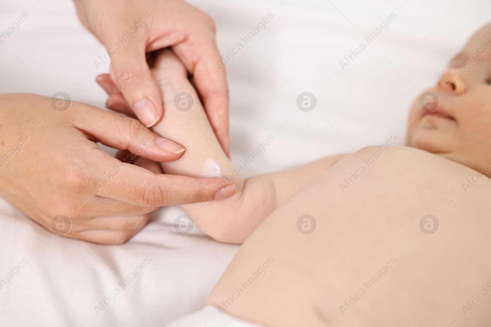 Photo of Woman applying body cream onto baby`s skin on bed, closeup