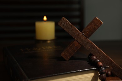 Cross, rosary beads, Bible and church candle on table, closeup