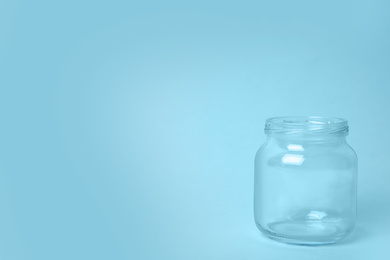 Photo of Open empty glass jar on light blue background, space for text