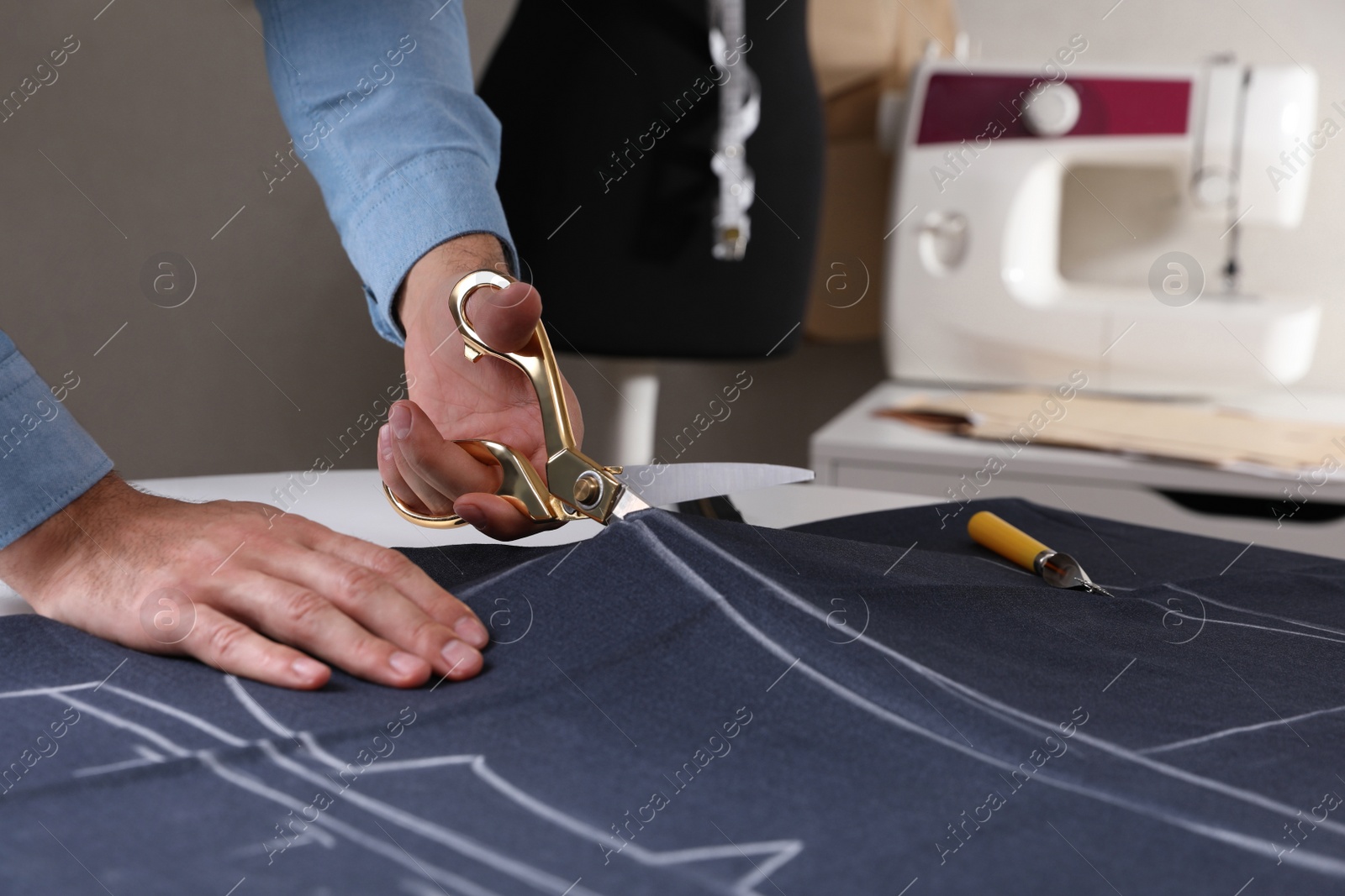 Photo of Tailor cutting fabric with scissors at table in atelier, closeup