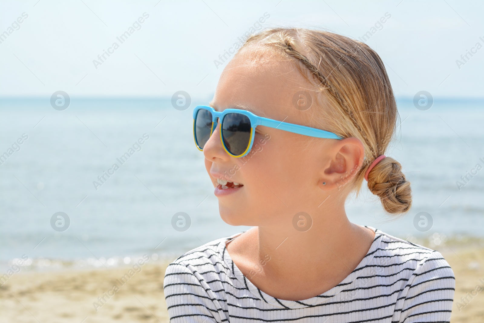 Photo of Little girl wearing sunglasses at beach on sunny day. Space for text