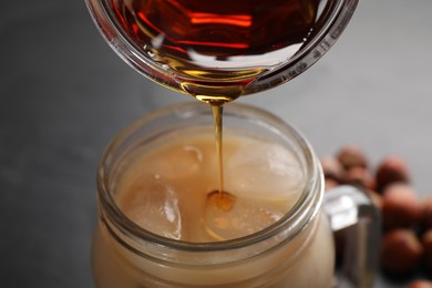 Pouring syrup into mason jar of tasty iced coffee on black table, closeup