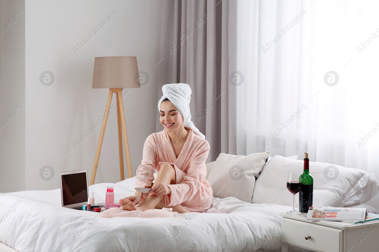 Photo of Beautiful young woman giving herself pedicure on bed at home