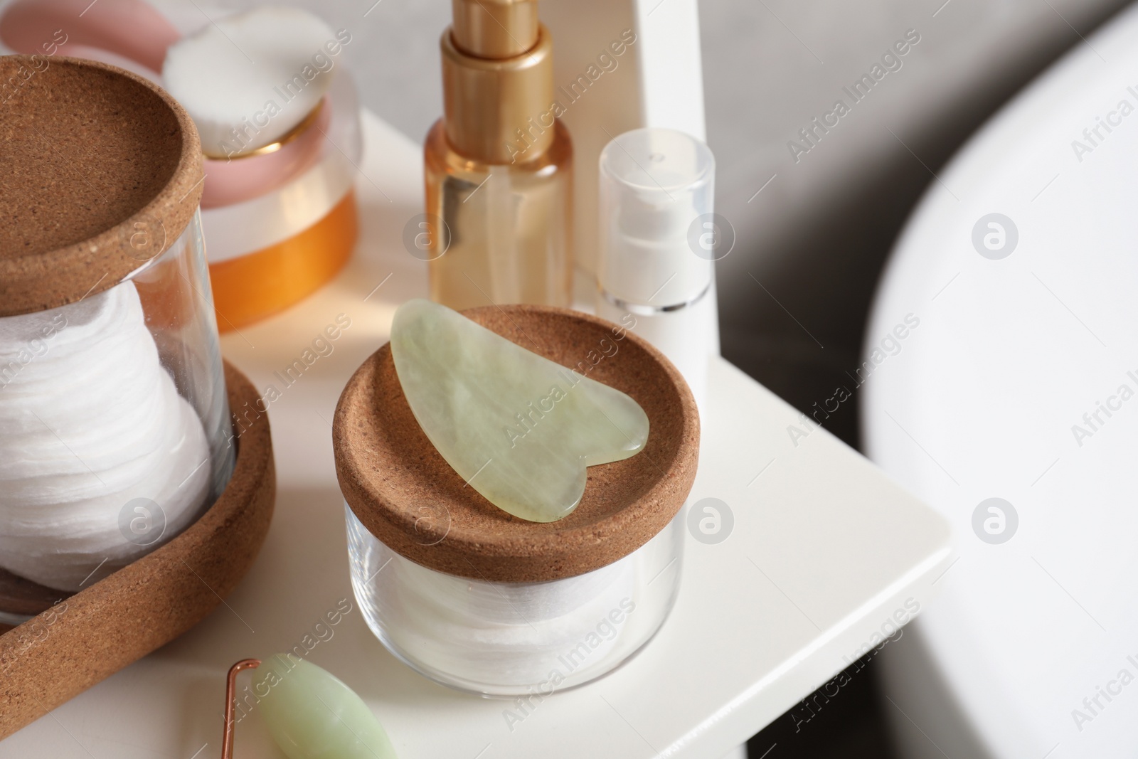 Photo of Jade gua sha tool and toiletries on white shelf