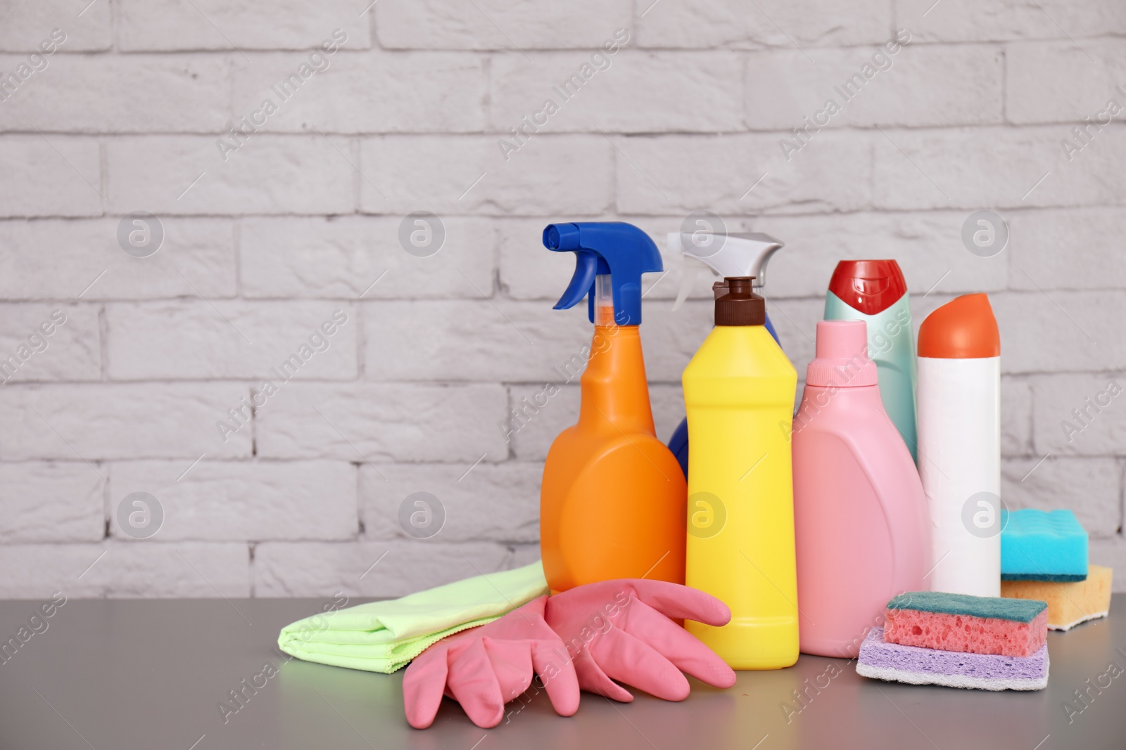 Photo of Set of cleaning supplies on table near brick wall