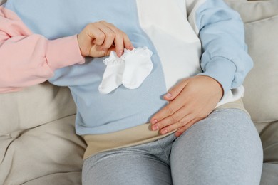 Pregnant woman sitting on sofa with baby socks, closeup