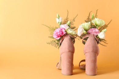 Photo of Stylish women's high heeled shoes with beautiful flowers on pale orange background, space for text
