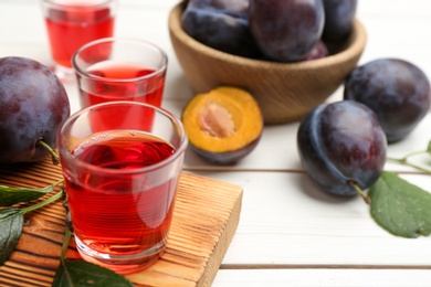 Photo of Delicious plum liquor and ripe fruits on white wooden table, closeup. Homemade strong alcoholic beverage