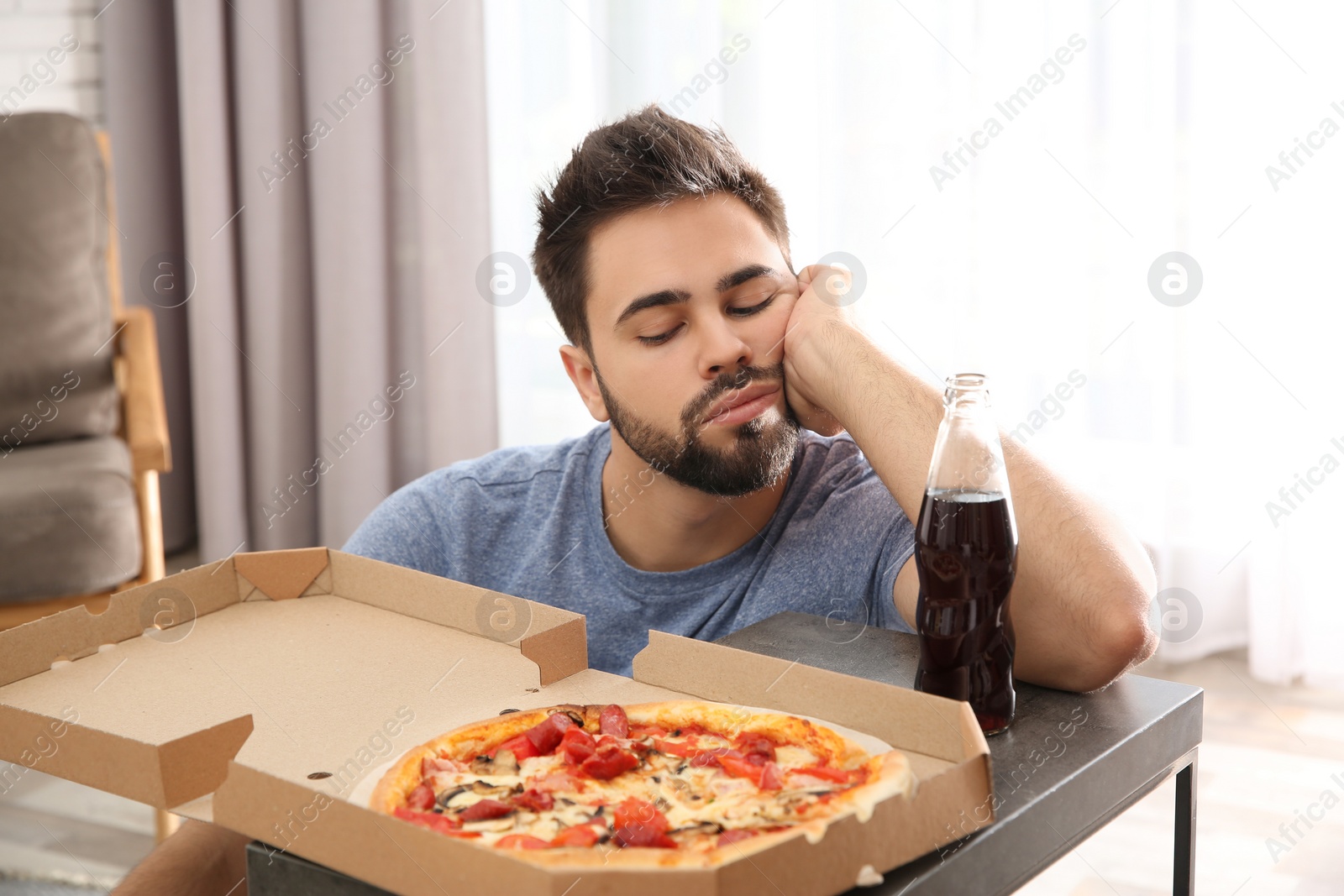 Photo of Lazy young man with pizza and drink at home