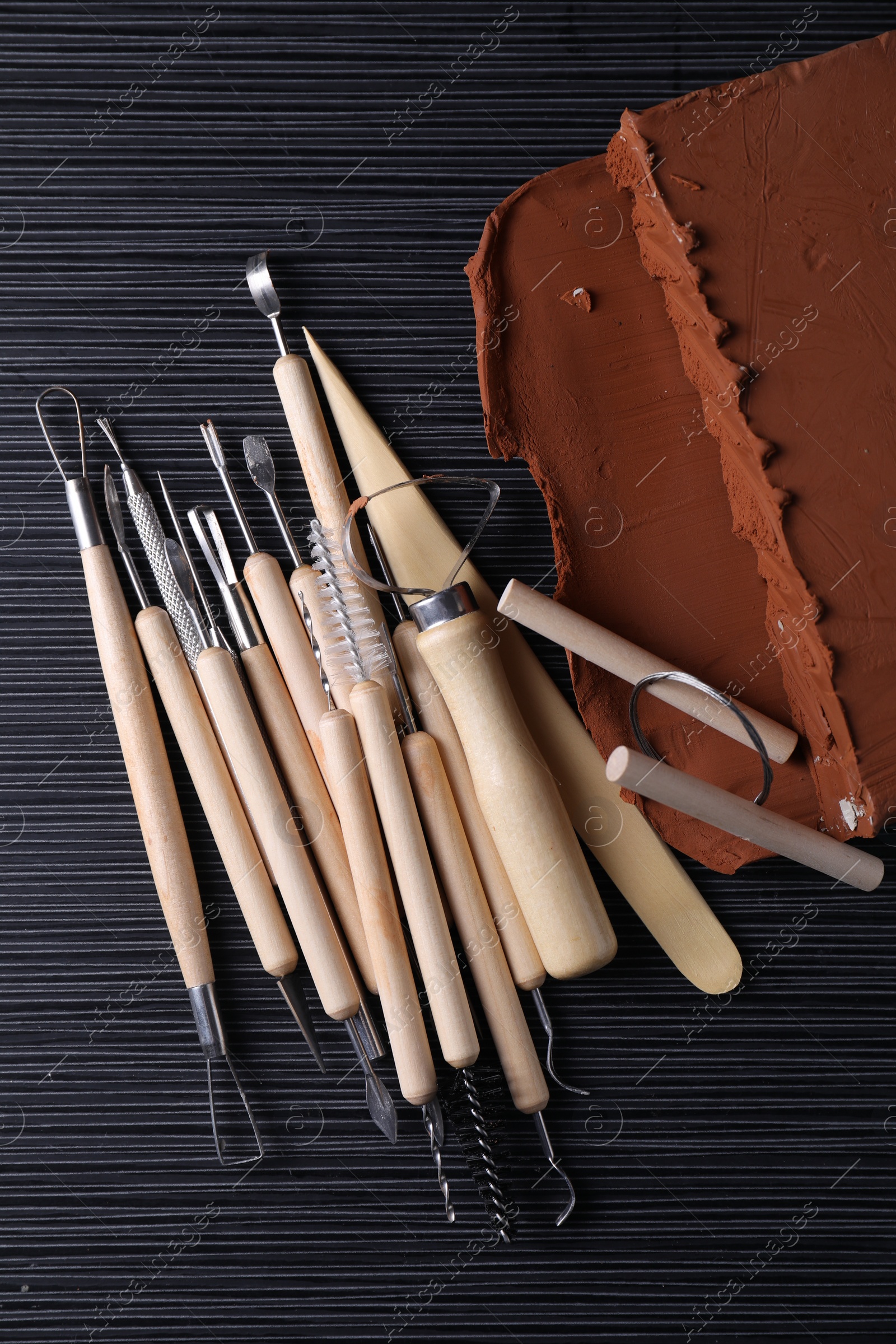 Photo of Clay and set of modeling tools on dark gray wooden table, flat lay