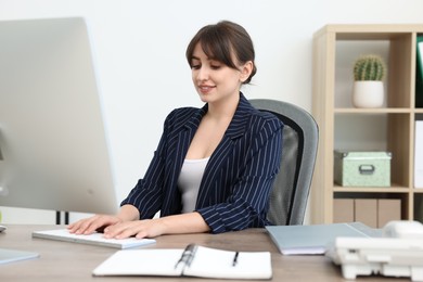 Smiling secretary typing on computer keyboard at table in office