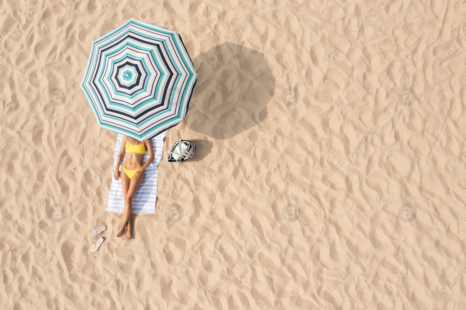 Image of Woman resting under striped beach umbrella at sandy coast, aerial view. Space for text