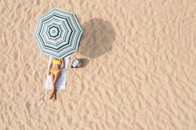 Image of Woman resting under striped beach umbrella at sandy coast, aerial view. Space for text