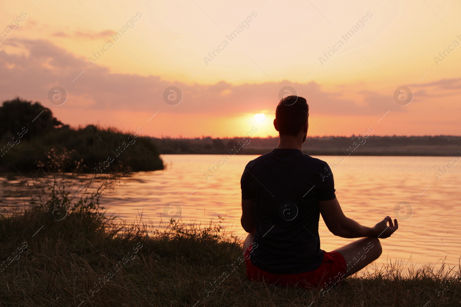 Photo of Man meditating near river at sunset, back view. Space for text