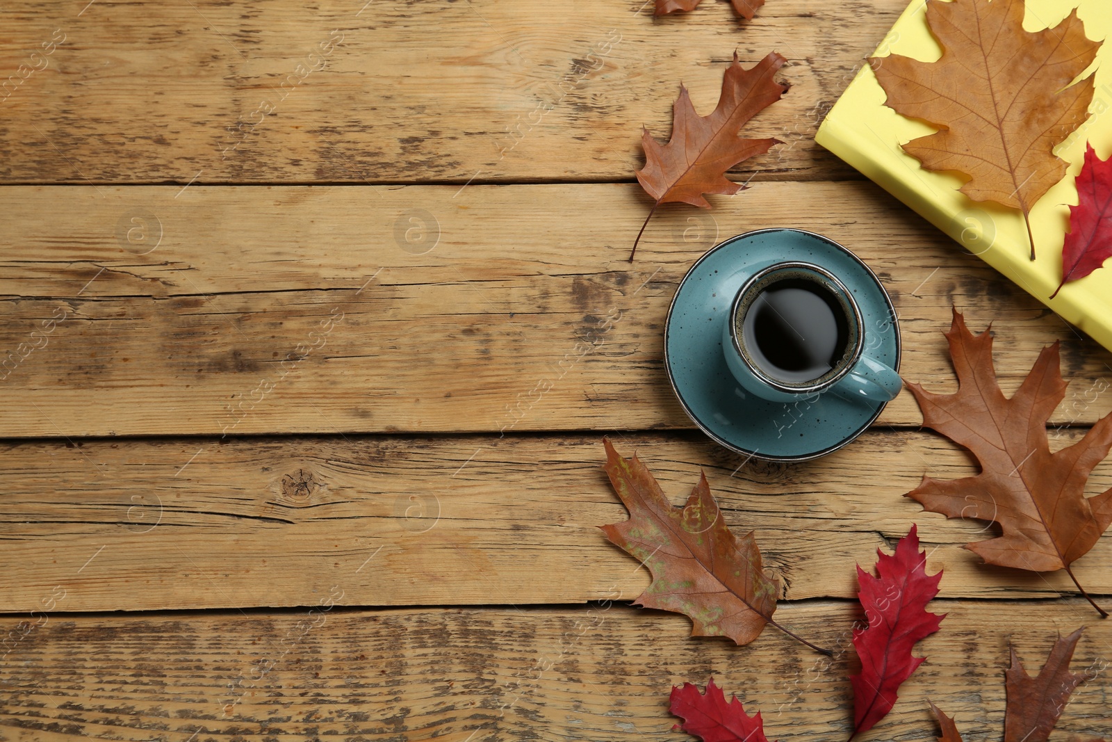 Photo of Cup of hot coffee, book and autumn leaves on wooden table, flat lay. Space for text