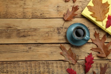 Cup of hot coffee, book and autumn leaves on wooden table, flat lay. Space for text