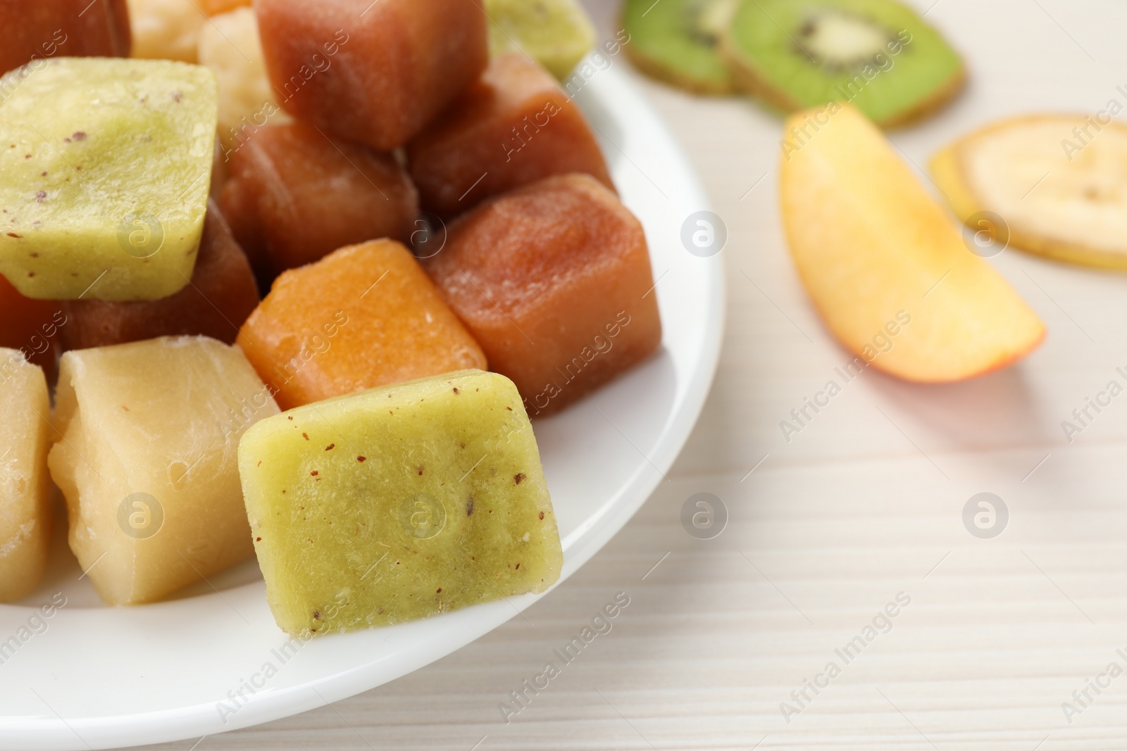 Photo of Different frozen fruit puree cubes and ingredients on white wooden table, closeup