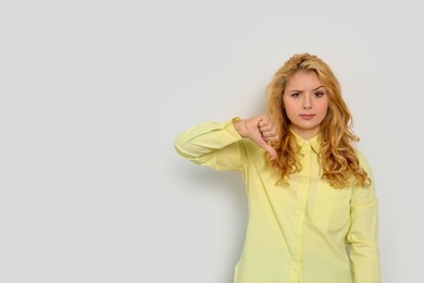 Photo of Dissatisfied young woman showing thumb down gesture on white background. Space for text