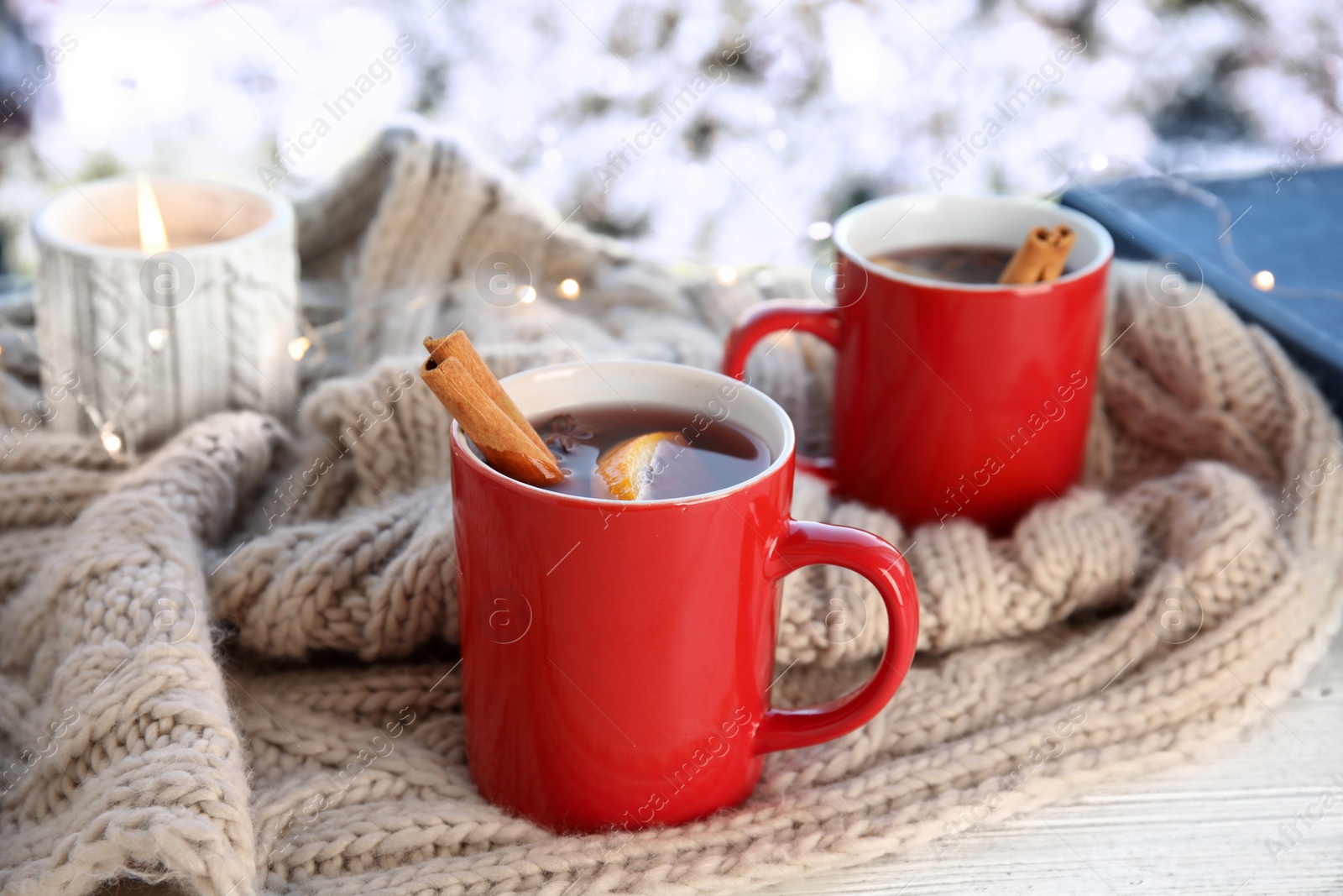 Photo of Cups of hot winter drink with scarf on window sill indoors