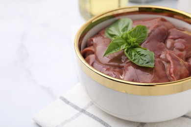 Photo of Bowl with raw chicken liver and basil on white marble table, closeup. Space for text