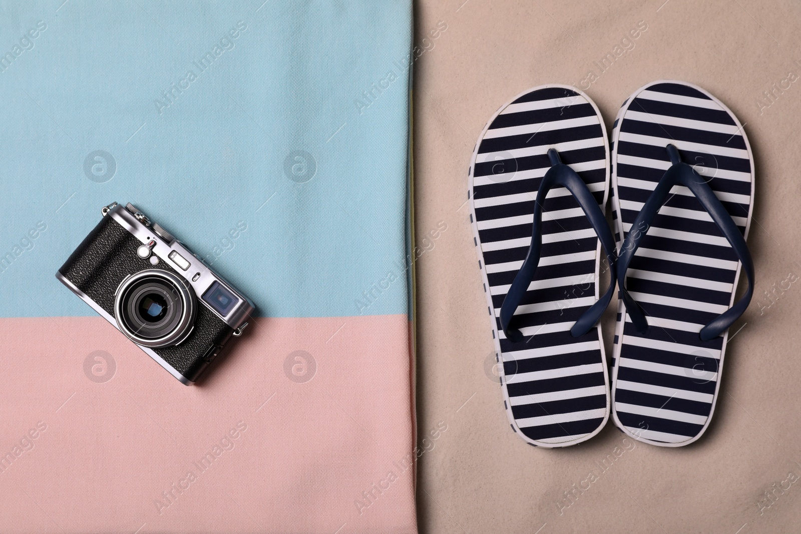 Photo of Beach towel, camera and flip flops on sand, flat lay