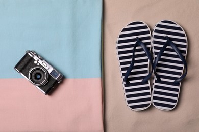 Photo of Beach towel, camera and flip flops on sand, flat lay