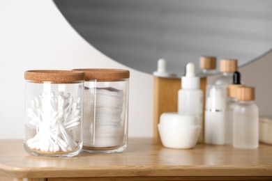 Glass jars with cotton swabs and pads near cosmetic products on dressing table
