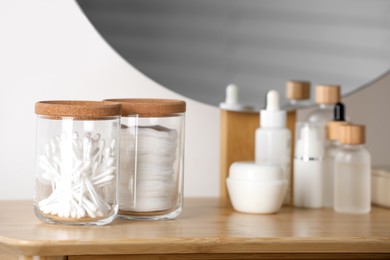 Photo of Glass jars with cotton swabs and pads near cosmetic products on dressing table