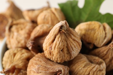 Photo of Tasty dried figs and green leaf in bowl, closeup