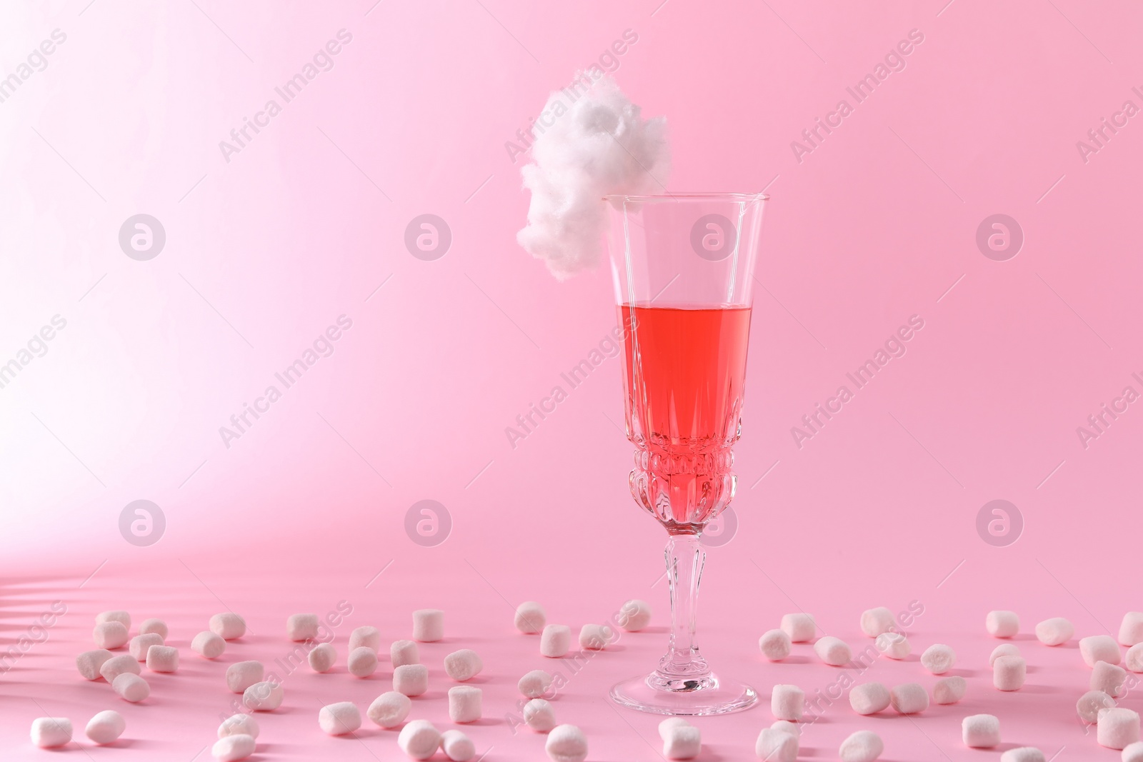 Photo of Tasty cocktail in glass decorated with cotton candy and marshmallows on pink background, space for text