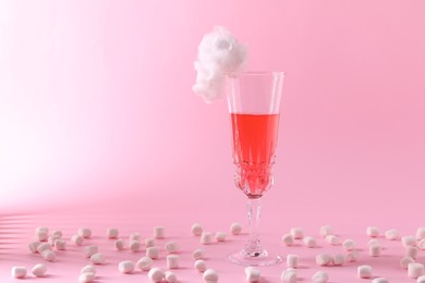 Photo of Tasty cocktail in glass decorated with cotton candy and marshmallows on pink background, space for text